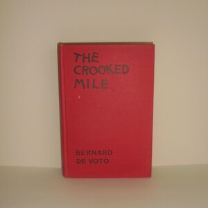 May include: A red hardcover book with the title "THE CROOKED MILE" and the author "BERNARD DE VOTO" printed on the front cover.