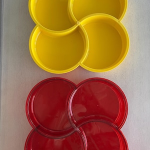 Puede incluir: Dos juegos de fuentes para servir de cuatro secciones. El juego superior es de color amarillo brillante y el juego inferior es rojo. Cada sección tiene forma redondeada y los juegos están conectados en un patrón floral. Los platos son de material brillante.