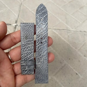 May include: A pair of gray watch straps with a textured, patterned surface. The straps are made of a durable material and feature multiple holes for adjustment. The watch straps are designed to be attached to a watch face.