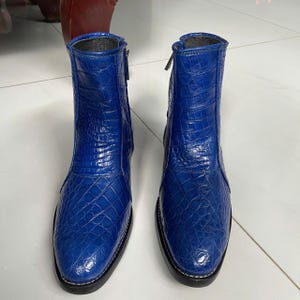 Könnte beinhalten: Ein Paar Stiefeletten in leuchtendem Königsblau mit einer strukturierten Krokodilleder-Optik. Die Stiefel haben eine abgerundete Zehenpartie, einen seitlichen Reißverschluss und eine schwarze Sohle mit sichtbaren weißen Nähten am Rand.