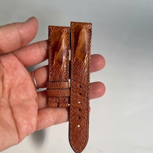 Puede incluir: Dos correas de reloj de cuero de avestruz marrón. Las correas son de un color marrón rojizo cálido con un patrón texturizado y con bultos. Una correa tiene una hebilla y la otra tiene varios agujeros para el cierre. Las correas son nuevas.