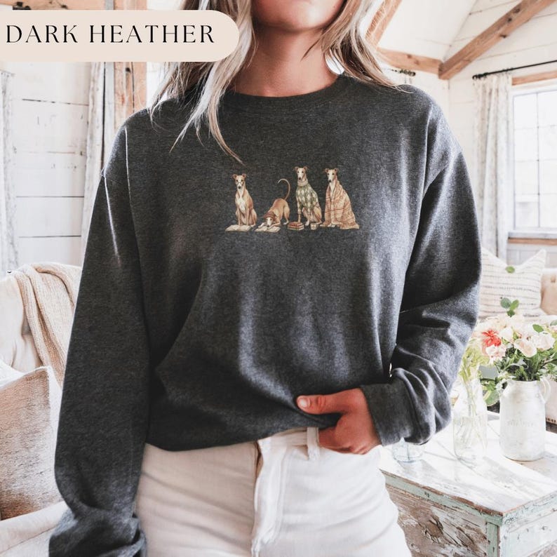 May include: Dark heather gray sweatshirt featuring an embroidered design of four dogs in various poses. One dog is wearing a plaid sweater, and another is draped in a blanket. The text "DARK HEATHER" is in the upper left corner.