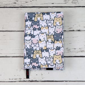 May include: A white notebook cover featuring a repeating pattern of cartoon cats wearing glasses. The cats are in various colours, including grey, white, pink, and yellow.