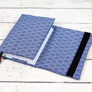 May include: A blue book cover with a wave pattern. The cover has a black elastic strap to keep it closed.