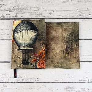 Peut inclure: Une couverture de livre en tissu marron et beige avec un ballon à air chaud vintage et un motif floral. La couverture a un fond beige avec un motif de plan délavé sur le côté droit.