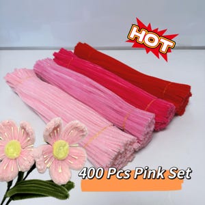 May include: Four bundles of pink and red pipe cleaners, with the text "400 Pcs Pink Set" and a "HOT" graphic. The pipe cleaners are in shades of light pink, medium pink, and red. Two pink flower decorations are in the lower left corner.