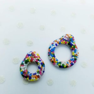 May include: Two colourful resin rings with a sprinkle pattern. The rings are different sizes and have a hole in the centre.