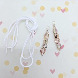 May include: Two strands of clear beads with a metallic sheen, each with a silver loop at the top. The beads are arranged in a graduated size, with the largest bead at the bottom and the smallest bead at the top. A white cord is also included.