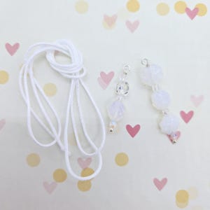 May include: Two white beaded necklace pendants with silver clasps and white cord. The pendants feature clear and opaque white beads.