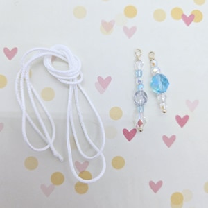 May include: Two strands of light blue and clear glass beads with gold accents on white cord. The cord is white and is tied in a knot.