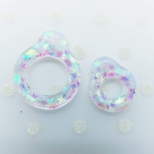 May include: Two clear resin rings with iridescent star-shaped glitter embedded inside. The rings are different sizes and are on a white background.