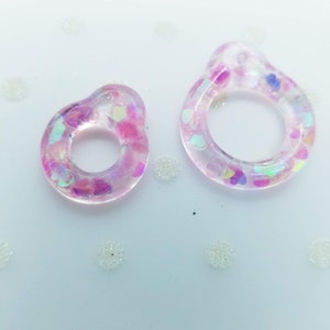 以下が含まれることがあります： ピンクと虹色のグリッターが埋め込まれた透明なレジン製のリングが2つ。リングはサイズが異なります。