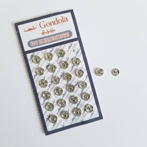 May include: A close-up of a pack of silver sew-on snap fasteners. The pack is labelled "Gondola Sew On Snapfasteners".