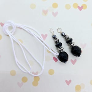May include: A pair of black and silver beaded earrings with a white cord.