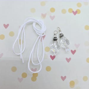 May include: Two clear crystal teardrop-shaped charms with silver accents and a white cord. The charms are on a white background with pink and yellow confetti.