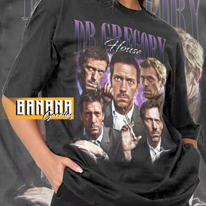 May include: Black unisex t-shirt with a graphic of Dr. Gregory House and the text "DR. GREGORY House". The shirt has a vintage design with a faded purple background and the "BANANA Gordas" logo.