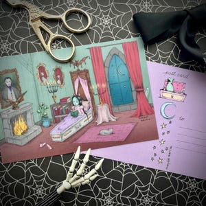 May include: A whimsical illustration of a gothic bedroom scene with a girl reading in a coffin bed. A postcard with a cat in a chest and a crescent moon is next to the illustration. A skeleton hand and scissors are also in the image.
