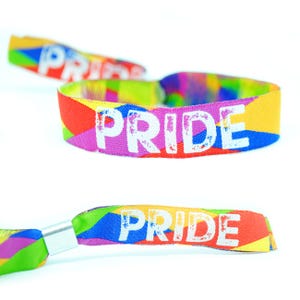 May include: Vibrant PRIDE wristbands displaying the word "PRIDE" in white. The bands showcase a rainbow design with red, orange, yellow, green, blue, and purple hues. The wristbands are made of a woven fabric.