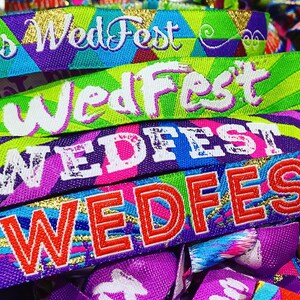 May include: A close-up of colorful wristbands with the text "WedFest" printed on them. The wristbands are made of woven fabric and have a variety of patterns and colors, including purple, blue, green, pink, and yellow.