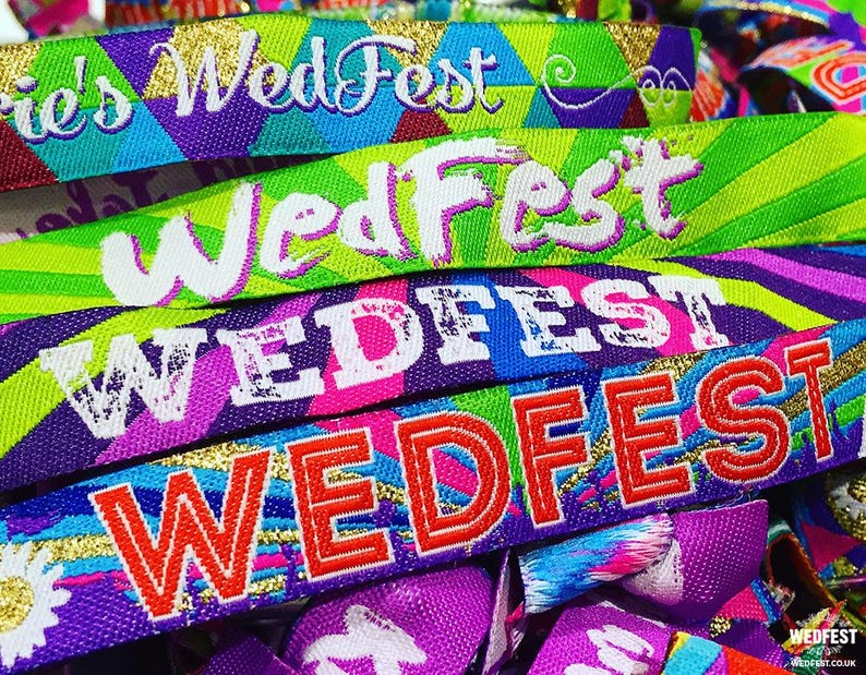 May include: A close-up of colorful wristbands with the text "WedFest" printed on them. The wristbands are made of woven fabric and have a variety of patterns and colors, including purple, blue, green, pink, and yellow.