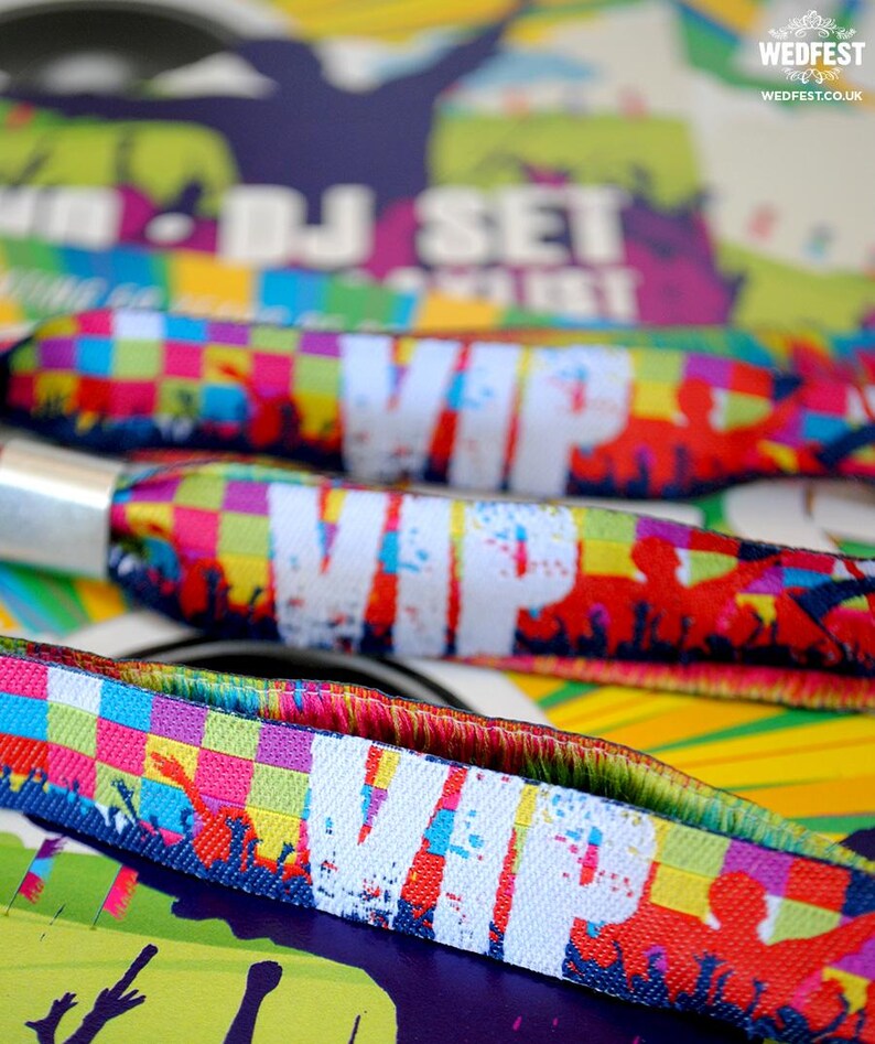 May include: Colorful wristbands with the word "VIP" printed in white. The wristbands have a checkered pattern and feature a crowd of people in the background.