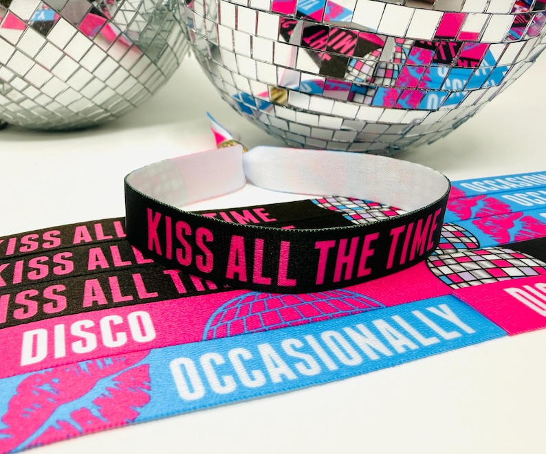 Może przedstawiać: Czarna opaska na nadgarstek z r&oacute;żowym napisem "KISS ALL THE TIME". Opaska leży na r&oacute;żowo-niebieskiej tkaninie we wzory ze słowami "DISCO" i "OCCASIONALLY". Dwie kule dyskotekowe w tle.