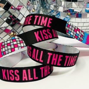 Może przedstawiać: Czarne opaski na nadgarstki z r&oacute;żowym napisem "KISS ALL THE TIME". Opaski mają wz&oacute;r kuli dyskotekowej i ust w kolorze r&oacute;żowym, niebieskim i białym. Tło z kulą dyskotekową.