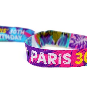 May include: A colorful wristband with the text "Paris 30th Festival" in white letters on a pink background. The wristband also has a tropical print with blue, green, yellow, and pink colors.