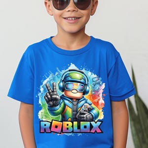 A smiling boy wearing a vibrant blue t-shirt with a colorful Roblox character wearing headphones and sunglasses with a large Roblox logo.