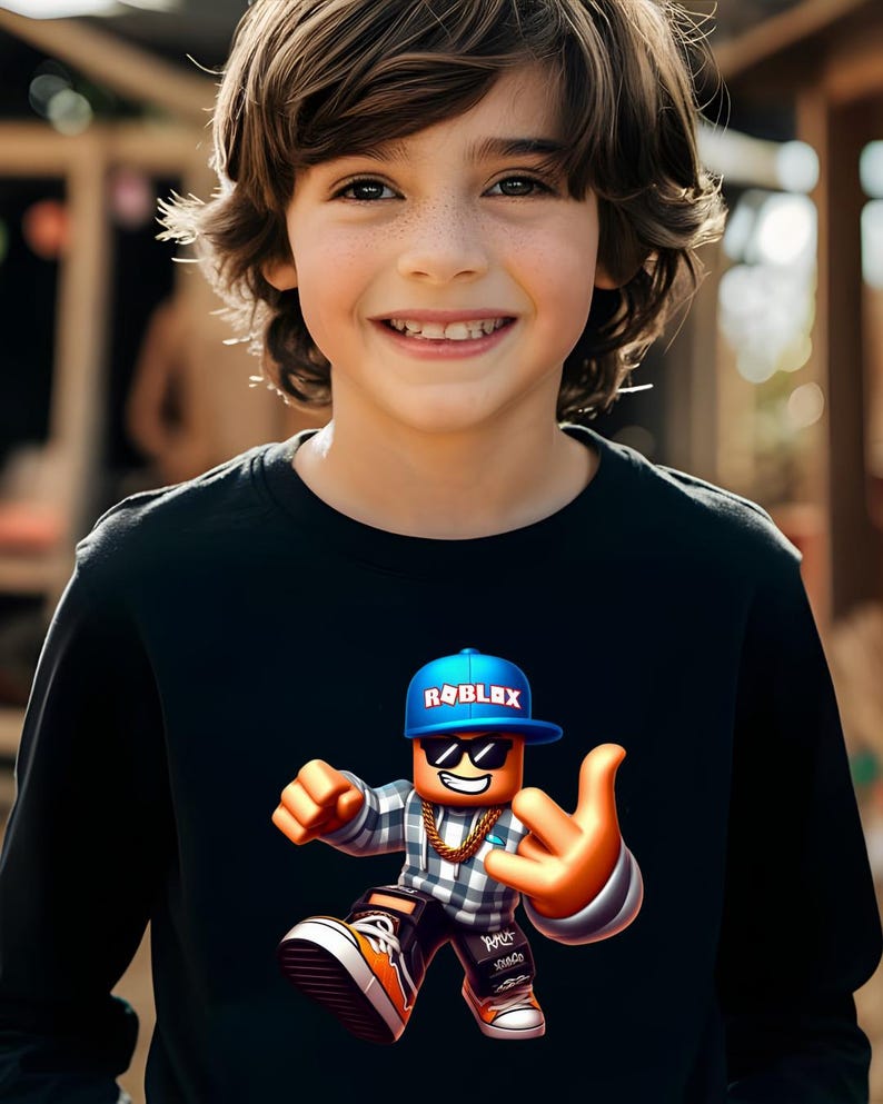 以下が含まれることがあります： 笑顔の子供が、Robloxのキャラクターのカラフルなグラフィックが描かれた黒い長袖シャツを着ています。キャラクターは「ROBLOX」の文字が入った青いキャップ、サングラス、金のチェーンを身につけています。キャラクターは手のジェスチャーをしています。