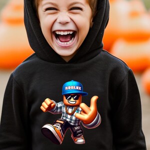 以下が含まれることがあります： 黒いフード付きスウェットシャツ。カラフルなRobloxキャラクターのグラフィックが特徴です。キャラクターは青いキャップ、サングラス、金のチェーンを身に着けています。「black」という単語が画像の下部にイタリック体で書かれています。