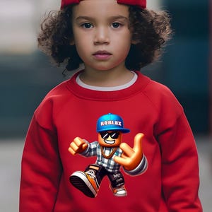以下が含まれることがあります： サングラスと青い帽子をかぶったRobloxのキャラクターのグラフィックが特徴の赤いスウェットシャツ。キャラクターは手のジェスチャーをしています。子供は赤い野球帽をかぶっています。