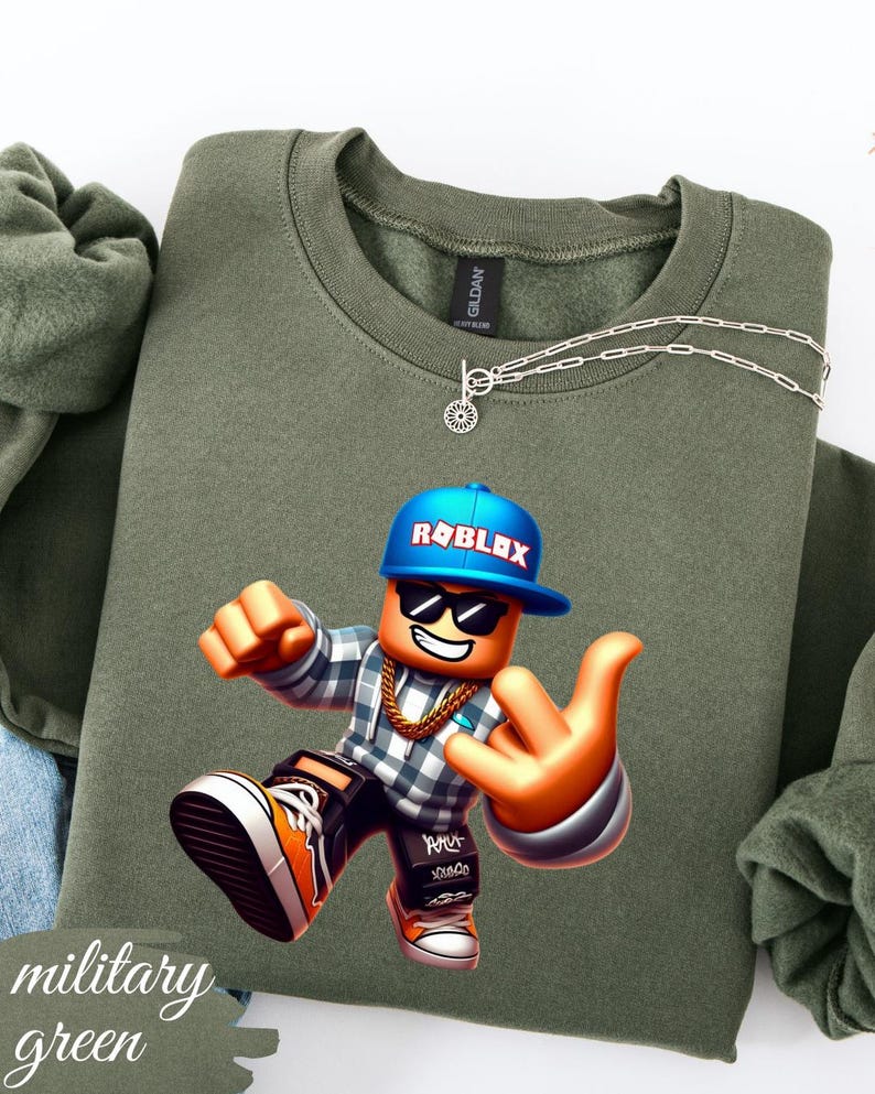 以下が含まれることがあります： ミリタリーグリーンのスウェットシャツ。カラフルなRobloxキャラクターのグラフィックが特徴です。キャラクターは青いキャップ、サングラス、金のチェーンを身に着けています。スウェットシャツはクルーネックで、シルバーのネックレスが付いています。「military green」の文字が左下に印刷されています。