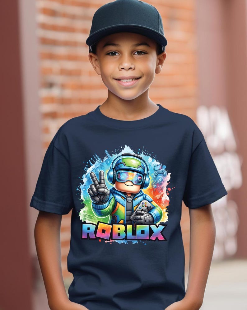K&ouml;nnte beinhalten: Ein marineblaues T-Shirt mit einem farbenfrohen Roblox-Grafikdesign. Die Grafik zeigt eine Figur mit Kopfh&ouml;rern und einem Gamecontroller, sowie das Roblox-Logo in einem Regenbogenverlauf. Die Person im Bild tr&auml;gt eine schwarze Baseballkappe.