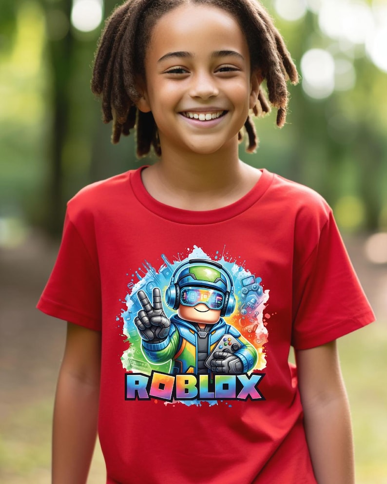 K&ouml;nnte beinhalten: Ein rotes T-Shirt mit einer farbenfrohen Grafik eines Roblox-Charakters mit Kopfh&ouml;rern, einem Controller und einem Friedenszeichen. Das Roblox-Logo ist in Regenbogenfarben dargestellt. Das T-Shirt wird von einer l&auml;chelnden Person getragen.
