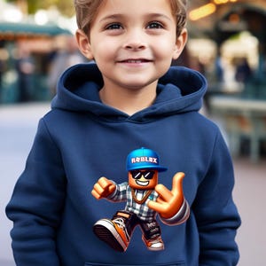 以下が含まれることがあります： ネイビーブルーのパーカー。ロブロックスのキャラクターが、ロブロックスのロゴが入った青いキャップ、サングラス、金のチェーンを身につけています。キャラクターは手のジェスチャーをしています。「navy」の文字が下部に筆記体で書かれています。