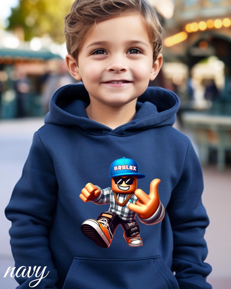 以下が含まれることがあります： ネイビーブルーのパーカー。ロブロックスのキャラクターが、ロブロックスのロゴが入った青いキャップ、サングラス、金のチェーンを身につけています。キャラクターは手のジェスチャーをしています。「navy」の文字が下部に筆記体で書かれています。