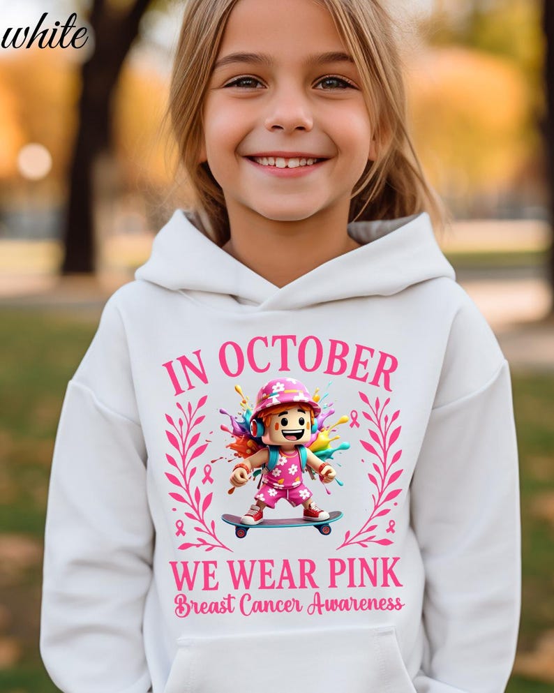 May include: White hoodie with the text "IN OCTOBER WE WEAR PINK Breast Cancer Awareness". The hoodie features a graphic of a character on a skateboard, surrounded by pink ribbons and floral elements. The word "white" is in the top left corner.