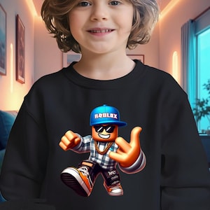 以下が含まれることがあります： 黒いスウェットシャツ。青い Roblox ロゴのキャップ、サングラス、金のチェーンを身に着けたカラフルな Roblox キャラクターが特徴です。キャラクターはハンドジェスチャーをしています。「black」の文字が下部に印刷されています。
