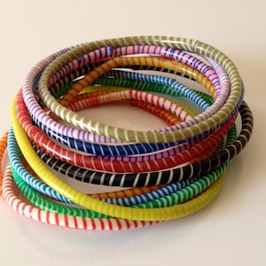 May include: A collection of colorful, striped bangles in various hues, including red, yellow, green, and blue. The bracelets are stacked together, showcasing a variety of patterns and designs. The bangles are made of a glossy material.