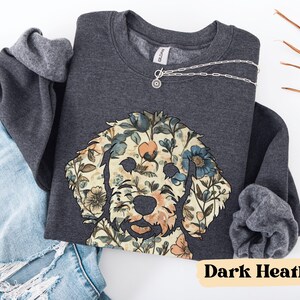 May include: Dark heather gray sweatshirt featuring a floral dog design. The dog's face is composed of various flowers in shades of blue, peach, and cream. The sweatshirt has a crew neck and long sleeves. A silver necklace with a pendant is visible.