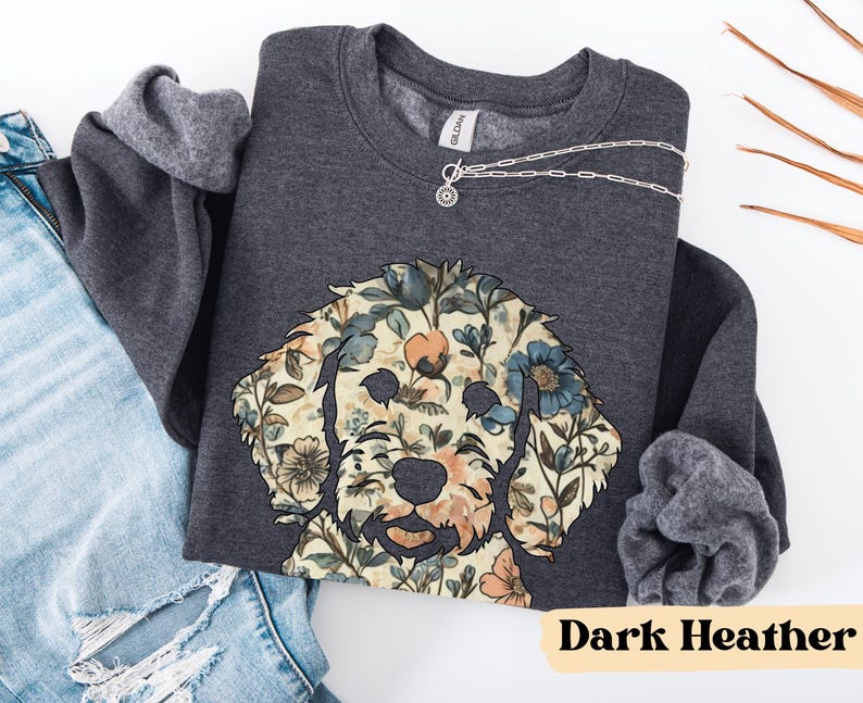May include: Dark heather gray sweatshirt featuring a floral dog design. The dog's face is composed of various flowers in shades of blue, peach, and cream. The sweatshirt has a crew neck and long sleeves. A silver necklace with a pendant is visible.