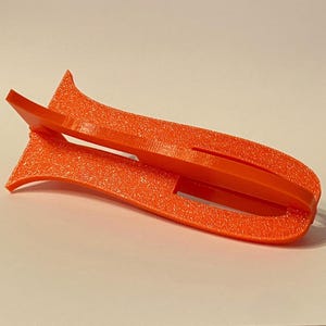 May include: An orange plastic phone stand with a textured surface. The stand is designed to hold a phone upright.