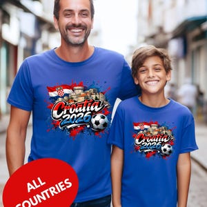 A man and a young boy are standing together, both wearing blue t-shirts with a graphic design featuring the text "Cromatia 2020" and a soccer ball.