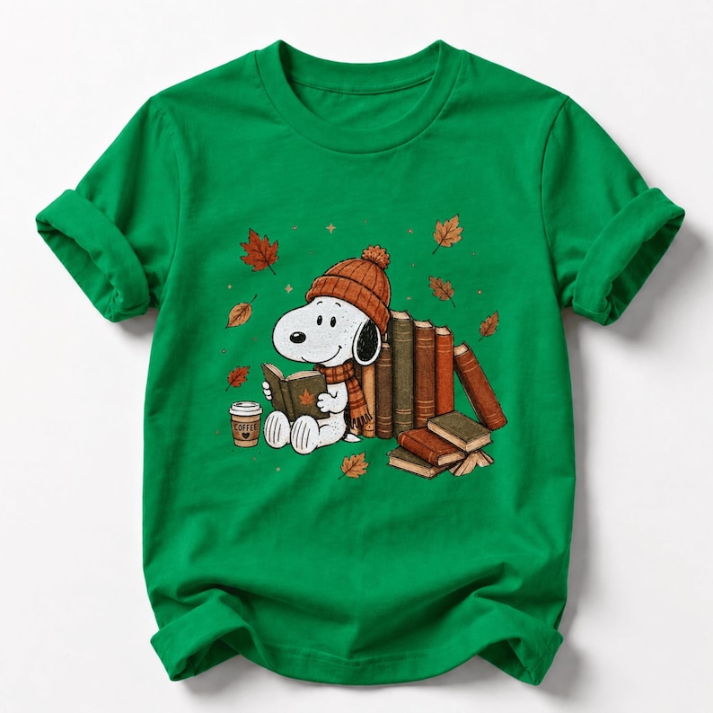 A green t-shirt with a cartoon image of a dog wearing a hat and scarf, sitting on a pile of books and holding a cup of coffee.
