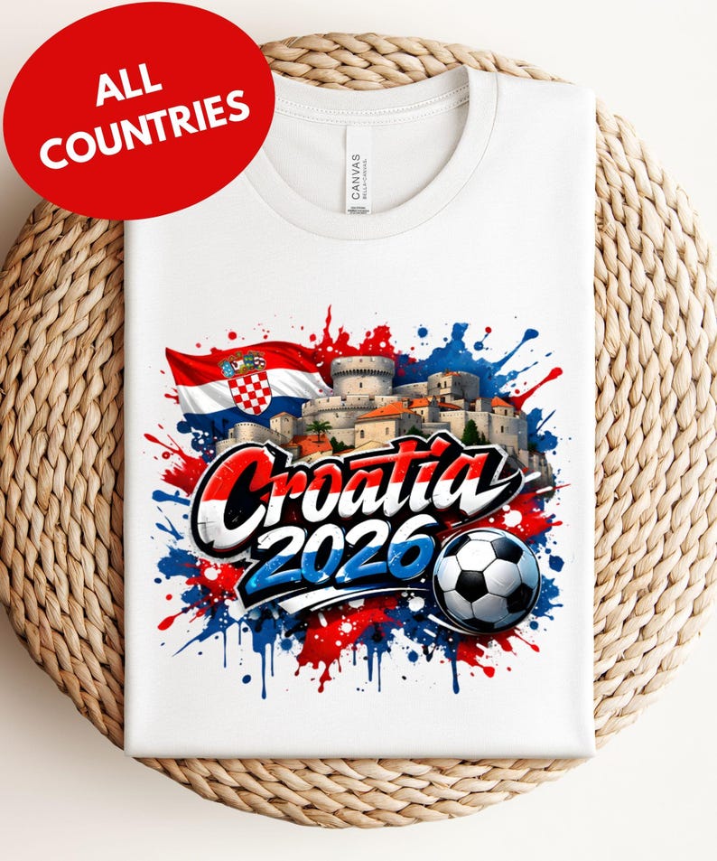 A white t-shirt with a graphic design featuring the text "Croatia 2026" and a soccer ball, surrounded by splashes of red, blue, and white colors.