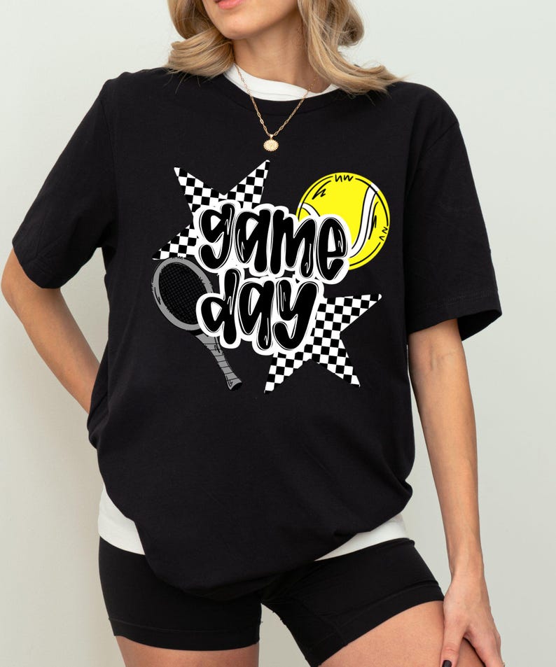 A woman wearing a black t-shirt with a graphic design featuring tennis equipment and the text "game day" printed on it.