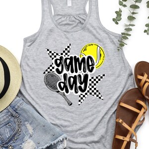 a gray tank top with a graphic design, a pair of denim shorts, a straw hat, and a pair of sandals, all laid out on a white background.