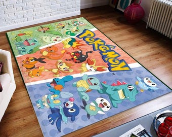 Op de afbeelding: Een rechthoekig vloerkleed met een levendig Pokemon-logo en diverse karakterillustraties, verdeeld in drie gekleurde secties: groen, oranje en blauw. Het ontwerp toont meerdere geanimeerde wezens over het gehele oppervlak.