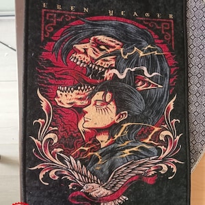 Pu&ograve; includere: Toppa ricamata nera e rossa con un'illustrazione dettagliata di un personaggio dell'anime L'Attacco dei Giganti. Il personaggio &egrave; circondato da fiamme e ha un uccello con un nastro rosso che vola sotto. Il testo "EREN YEAGER" &egrave; scritto in oro nella parte superiore della toppa.